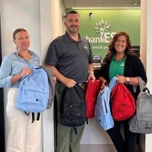 Bank employees holding backpacks filled with school supplies for a local drive.